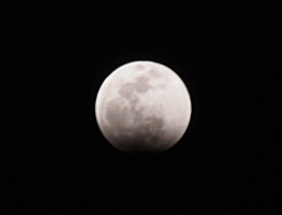 [A grey and white image of the full moon (slightly out of focus) which has a black shadow covering the bottom lip of the sphere and a dark greying which seems to extend about a quarter fof the way up the sphere although the mountains and valleys are still visible through the shadow.]